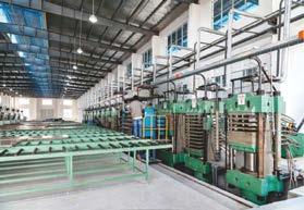 Large industrial facility with green hydraulic presses and conveyor systems for flooring production.