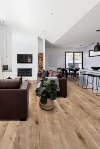 Open-plan living area with natural wooden flooring, brown leather sofas, indoor plants, a modern fireplace, and a dining area with a kitchen island.