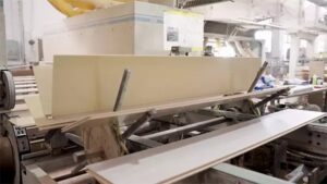 Wooden planks being processed on an industrial machine in a flooring manufacturing factory.