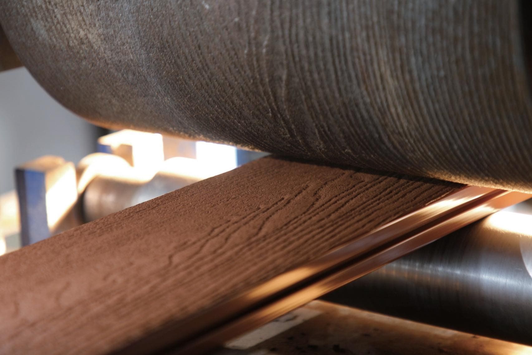 Close-up of a wood-like textured plank being processed through industrial rollers during manufacturing.