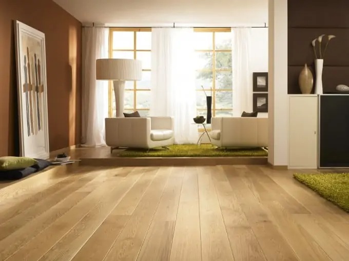 Büyük pencereli, beyaz mobilyalı ve doğal açık meşe laminat zeminli modern oturma odası.