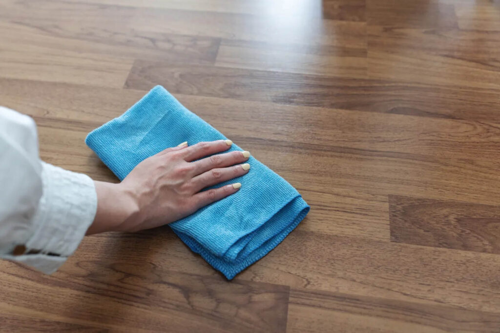 Temizlik veya cilalama için ahşap bir zeminin mavi mikrofiber bezle elle silinmesi.