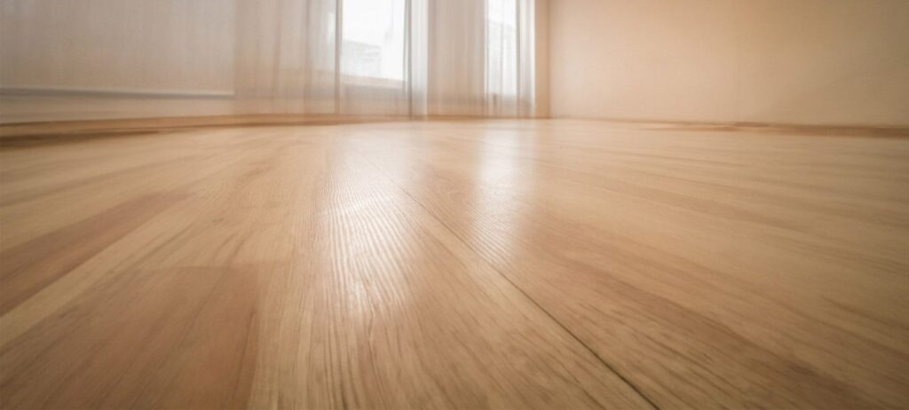 Close-up view of empty room with smooth, light oak laminate flooring and natural light from large windows.