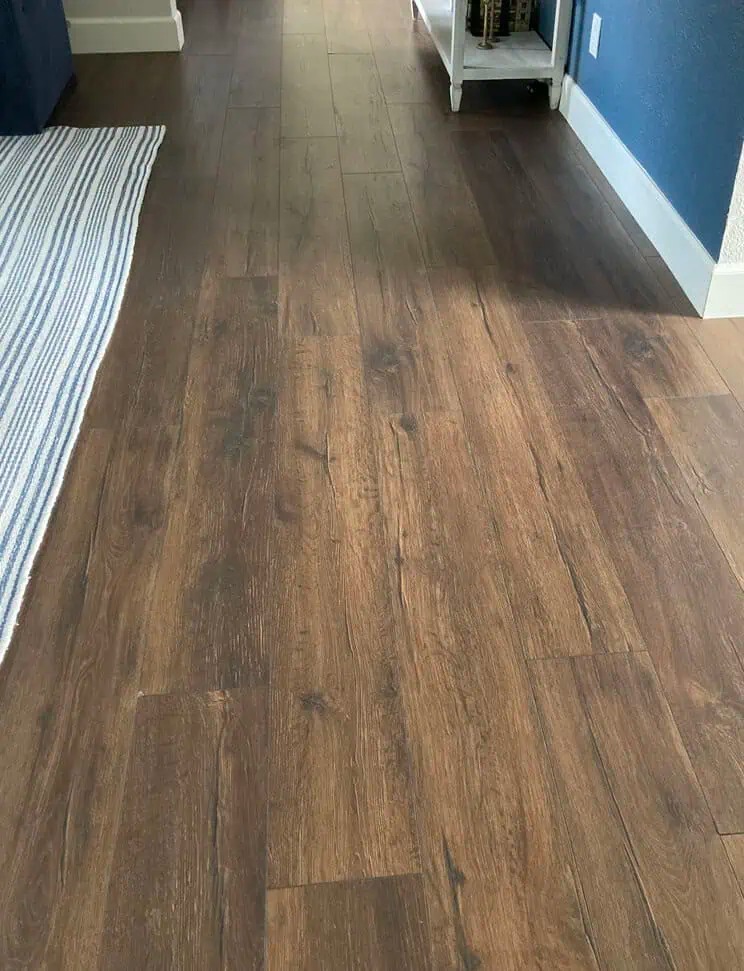 Suelo vinílico SPC en acabado madera marrón medio instalado en un vestíbulo residencial con rodapiés blancos.