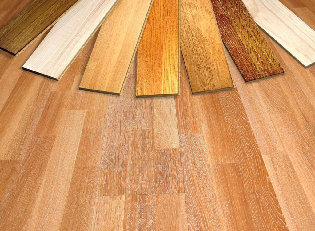 Various laminate wood flooring samples arranged in a fan shape on a wooden surface, showcasing different shades and grain patterns.