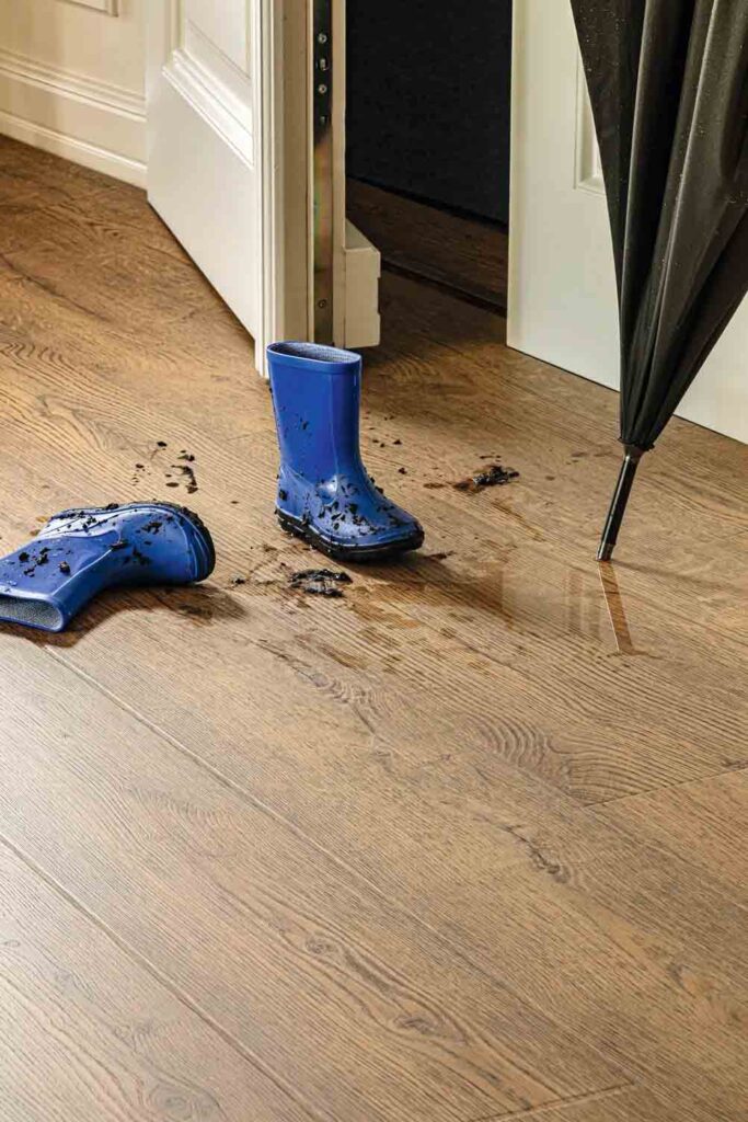 Suelo impermeable SPC con botas de lluvia azules embarradas y un paraguas en la superficie cerca de una puerta abierta.