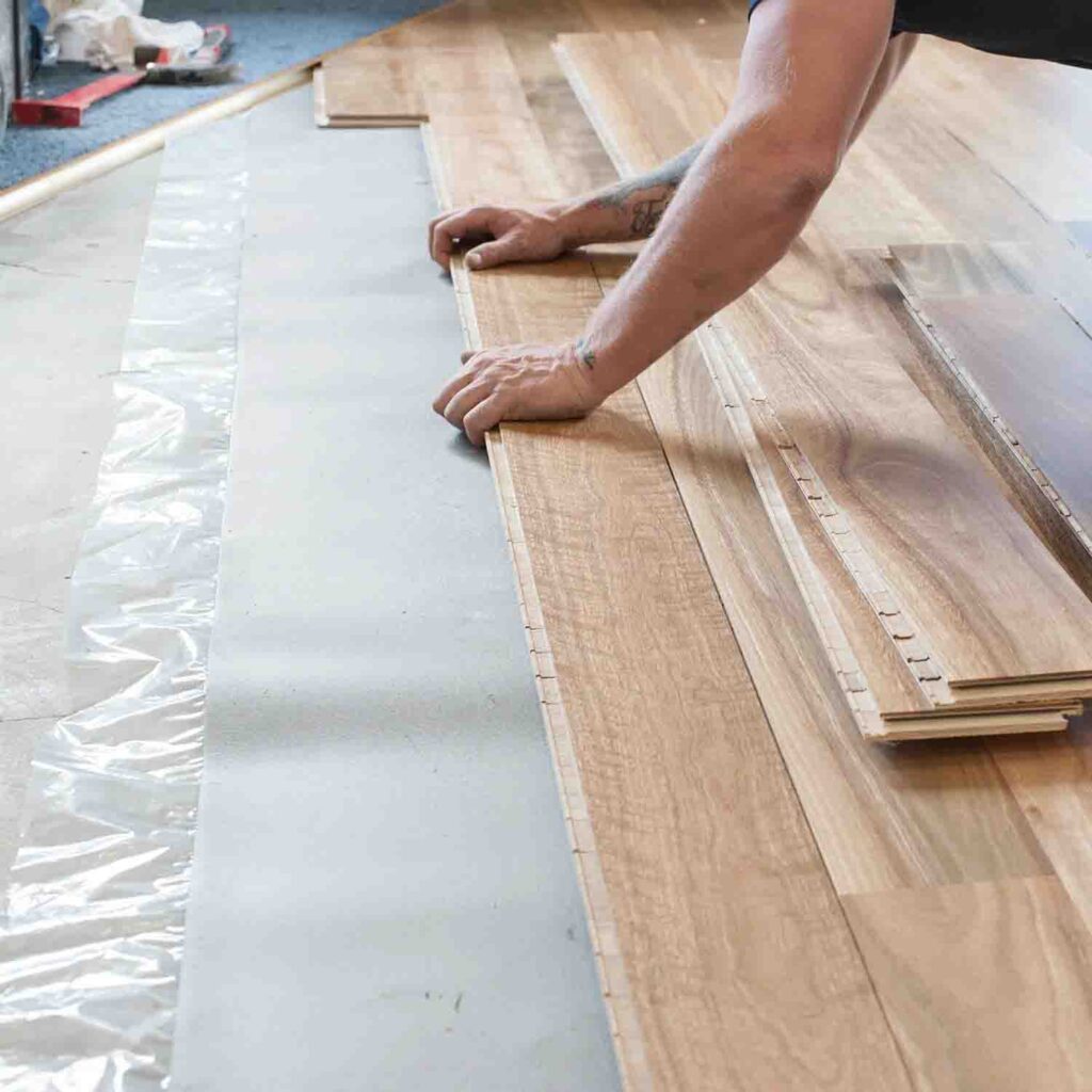 Worker installing laminate flooring over foam underlayment layer