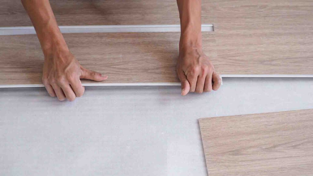 Hands installing light wood SPC flooring planks on underlayment