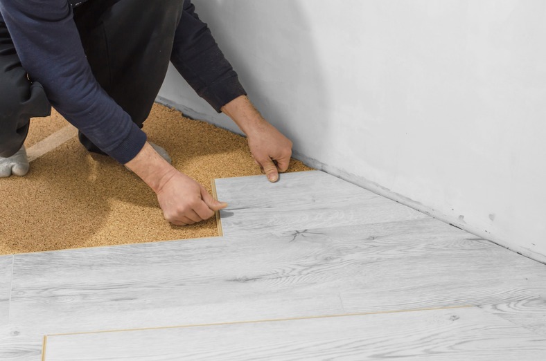 Installing gray wood grain SPC flooring over cork underlayment.